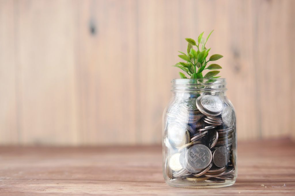 A jar full of coins with a plant sprout coming out of the top, representing investment growth